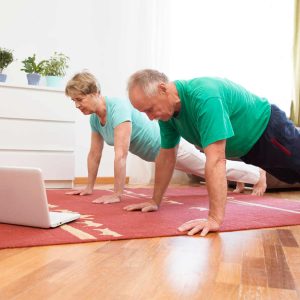 active senior couple is doing fitness training  in living room at home with laptop.  Remote Workouts.  home-based gym. home fitness, activewear.