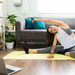 Attractive woman with a healthy lifestyle watching a video tutorial. Active woman doing stretching exercises with an online video on her laptop